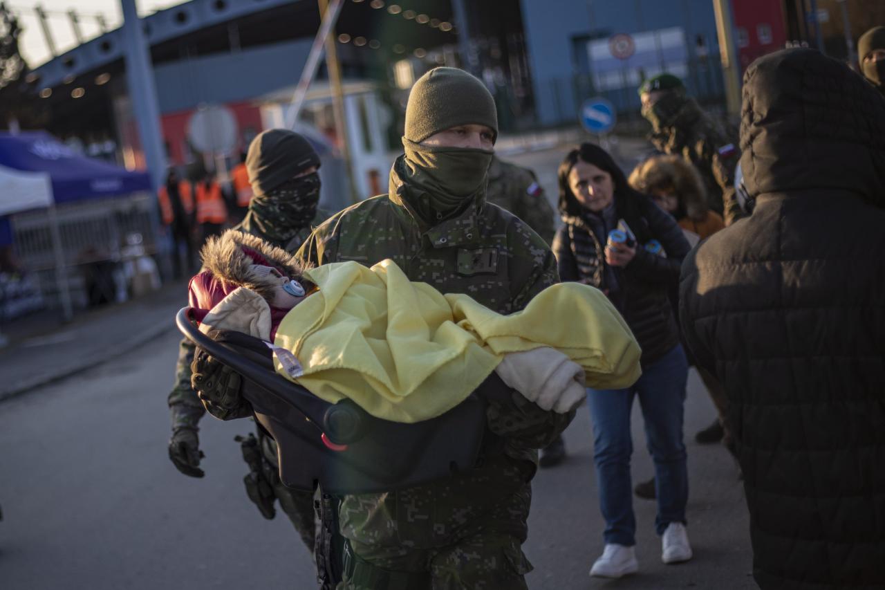 Un soldado eslovaco lleva a un niño en un asiento de automóvil cuando los fugitivos de Ucrania llegan a Eslovaquia.