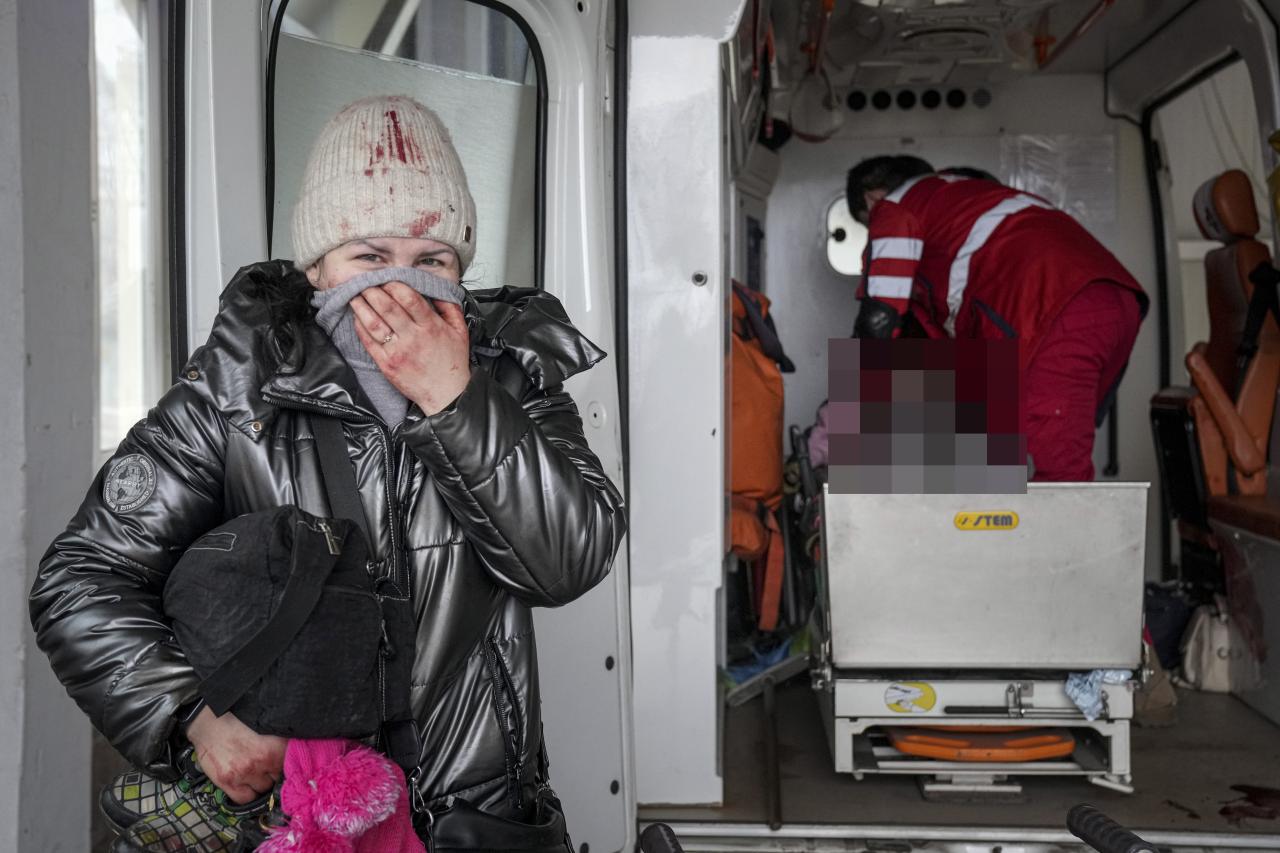 Una madre desesperada, ensangrentada y con un pañuelo rosa, espera frente a la ambulancia.