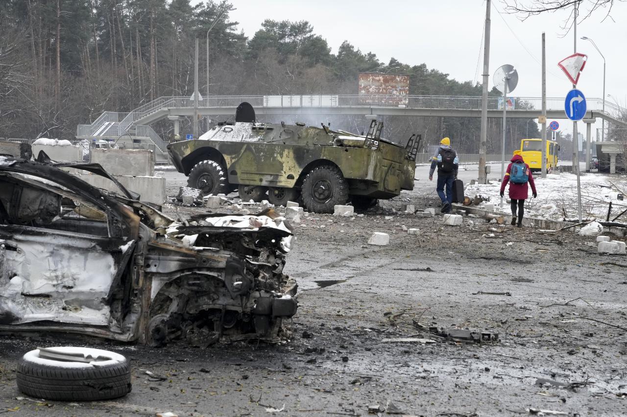 La gente camina junto a un vehículo dañado y un vehículo blindado en el puesto de control en Brovary, cerca de Kiev.