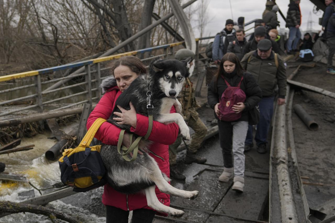 Una mujer carga un perro mientras cruza el río Irpin bajo un puente destruido por los ataques aéreos rusos.