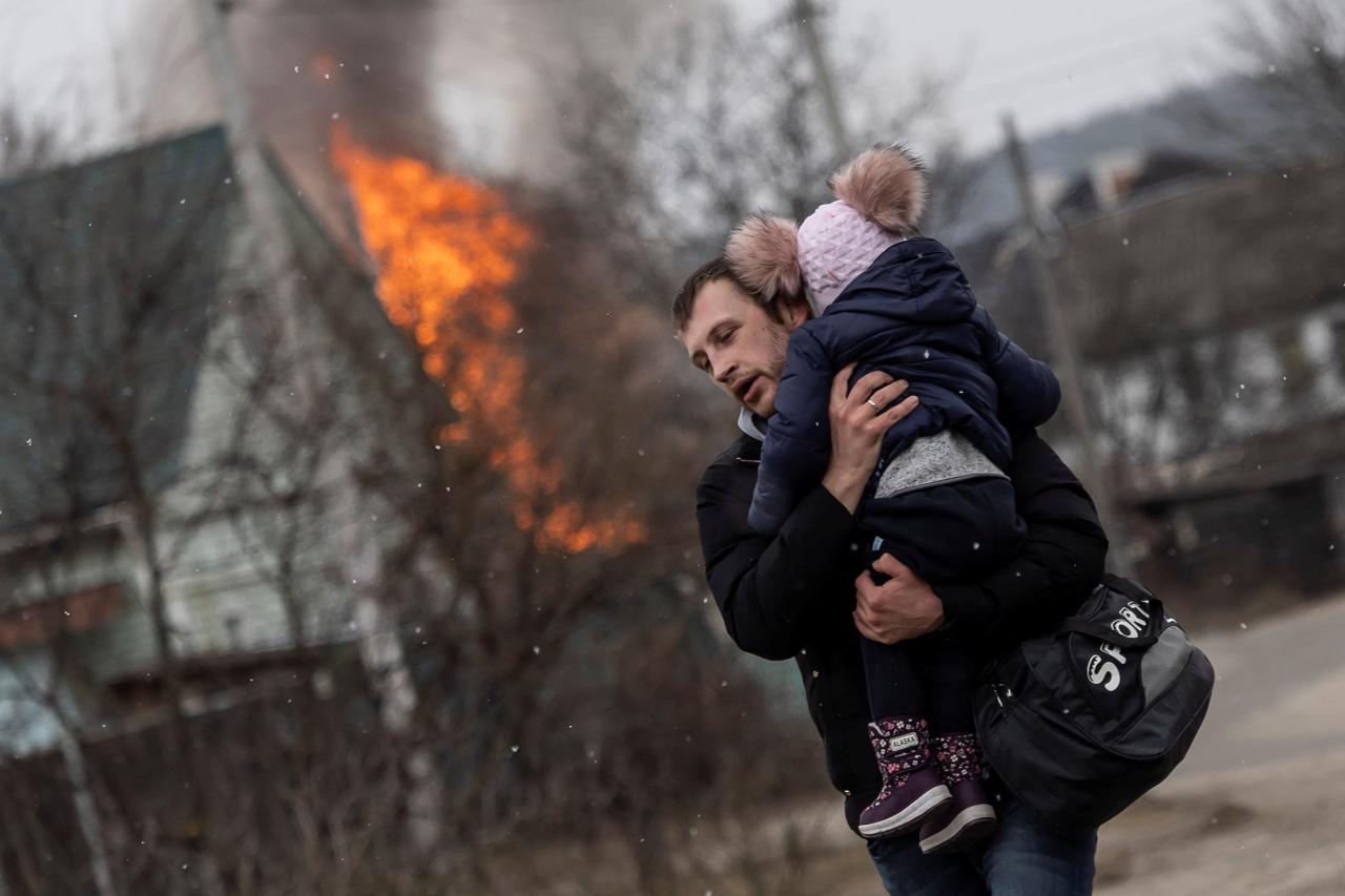 El padre lleva a su hija en brazos mientras el fuego arde detrás de ellos.