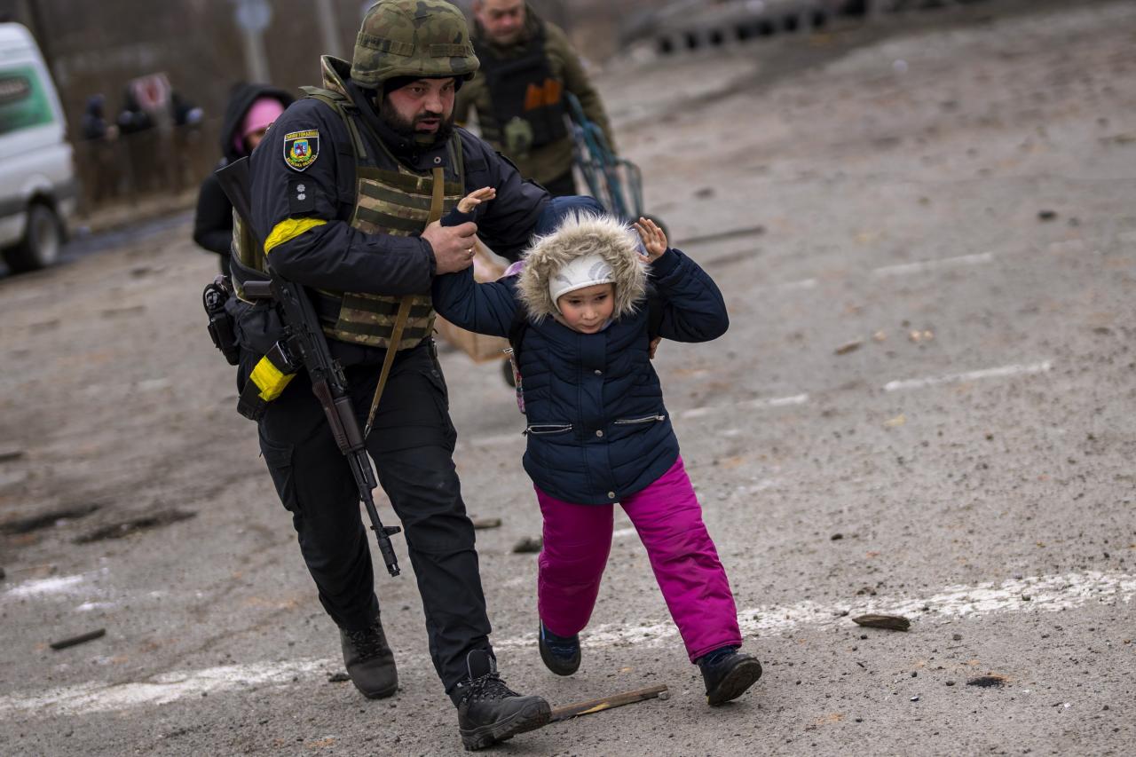 Un policía ucraniano en Irpin corre con un niño cuando la artillería hace eco cerca