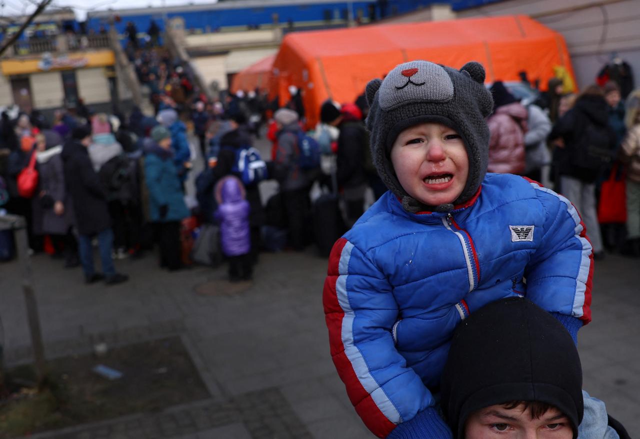 Un niño llora sentado sobre los hombros de su hermano mientras buscan a su madre frente a la estación de tren de Lviv.