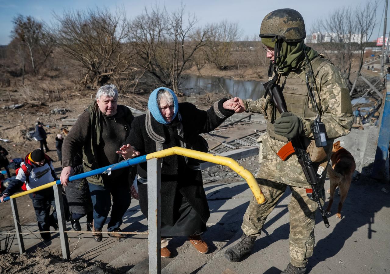 Un miembro de las fuerzas ucranianas ayuda a una mujer a cruzar el río Irpin durante su evacuación.