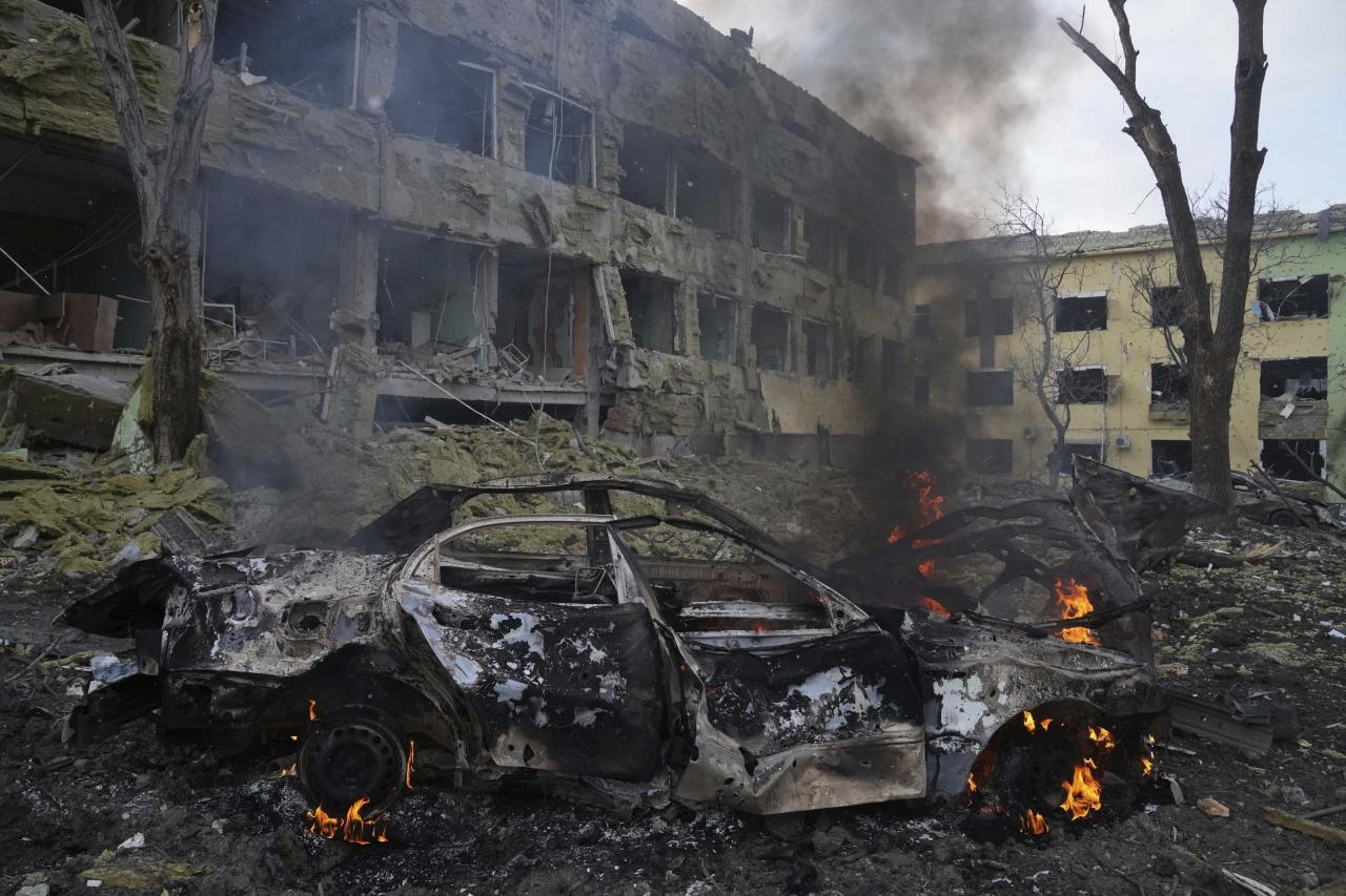 Un automóvil arde al costado del hospital de maternidad, que fue destruido por los bombardeos en Mariupol