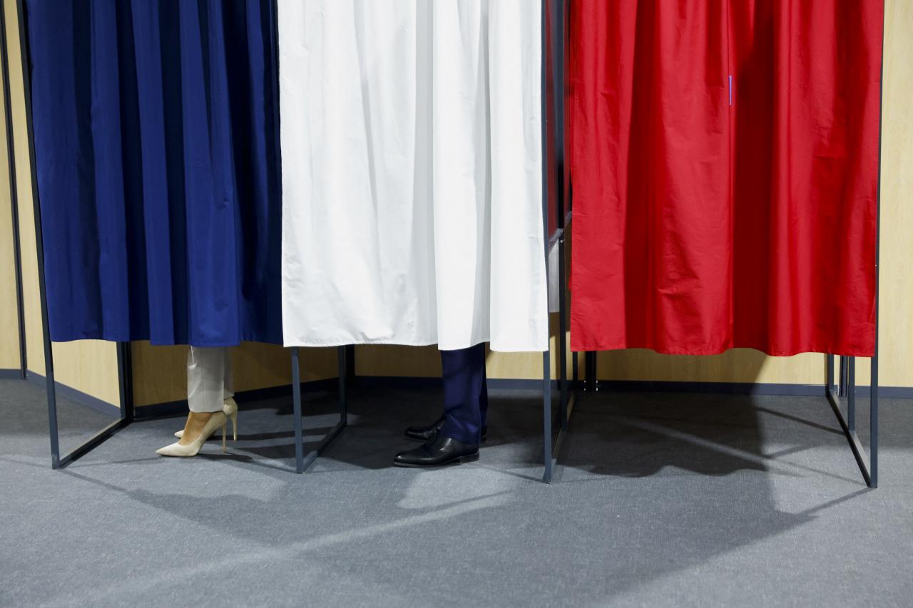 El presidente francés Emmanuel Macron y su esposa Brigitte Macron están de pie en las cabinas de votación.