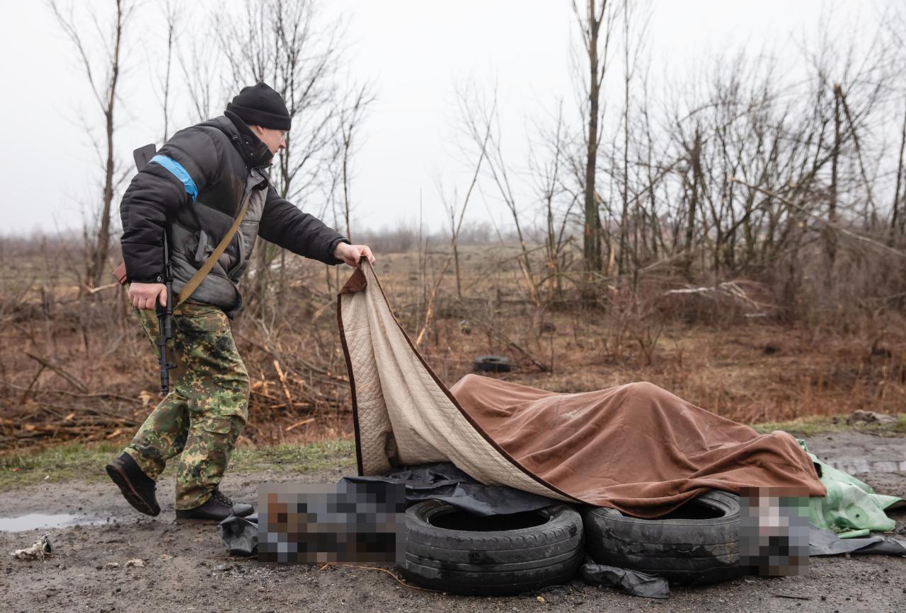 Las fuerzas de defensa civil observan a cuatro civiles muertos al costado de una carretera bajo una manta cerca de Kiev.
