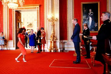 Mel B sonríe mientras hace una reverencia frente a William mientras recibe su MBE frente a su orgullosa madre