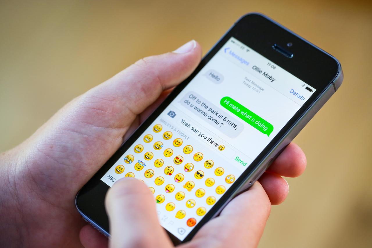 GNG8YX Adolescente usando emoticones mientras envía mensajes de texto en su iPhone